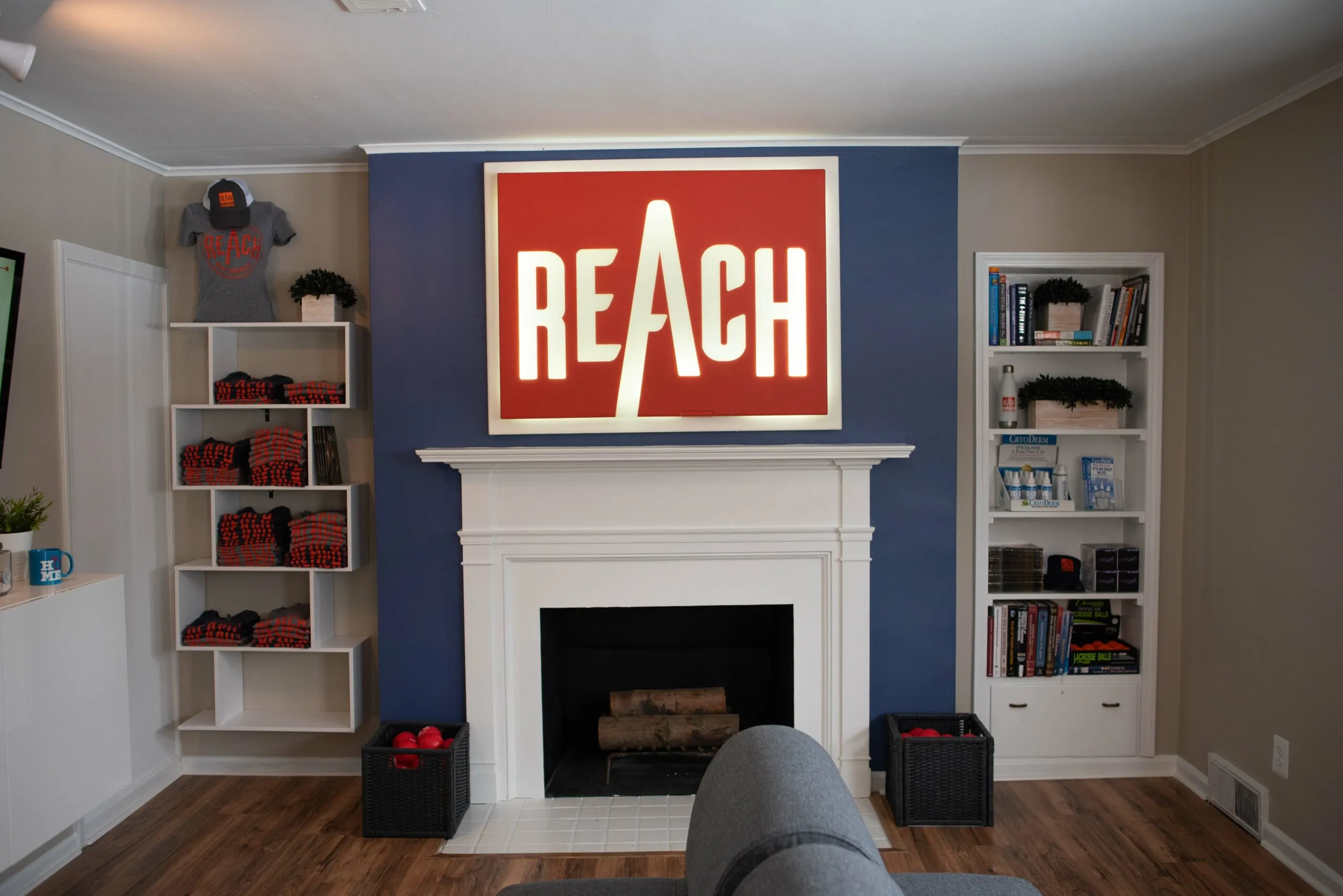 The REACH Rehab + Chiropractic waiting room in Plymouth, MI, with the illuminated REACH sign above the fireplace and shelves of branded apparel