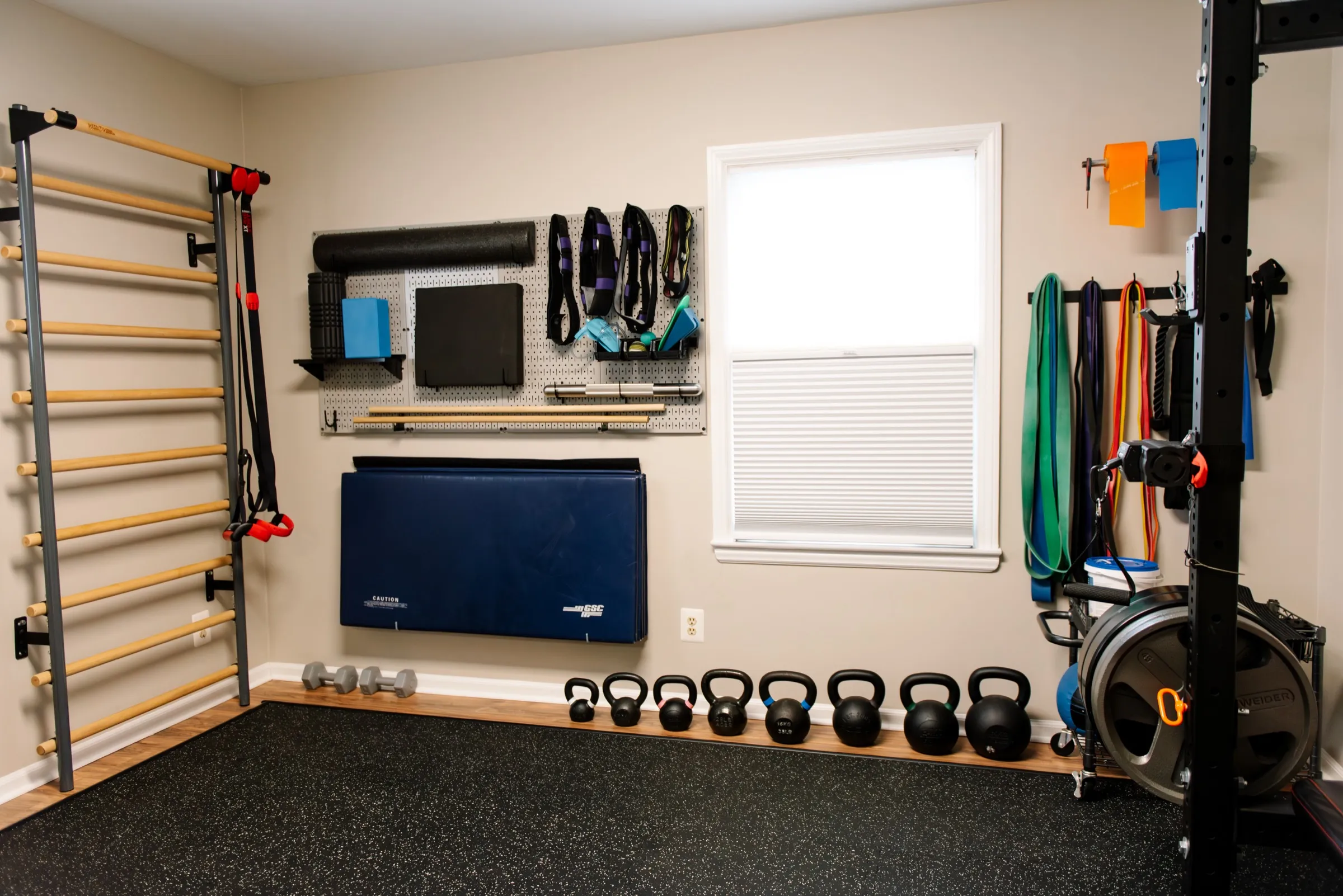 The REACH Rehab + Chiropractic gym room in Plymouth, MI, with kettlebells, resistance bands, and a rack of weight plates, no patient present