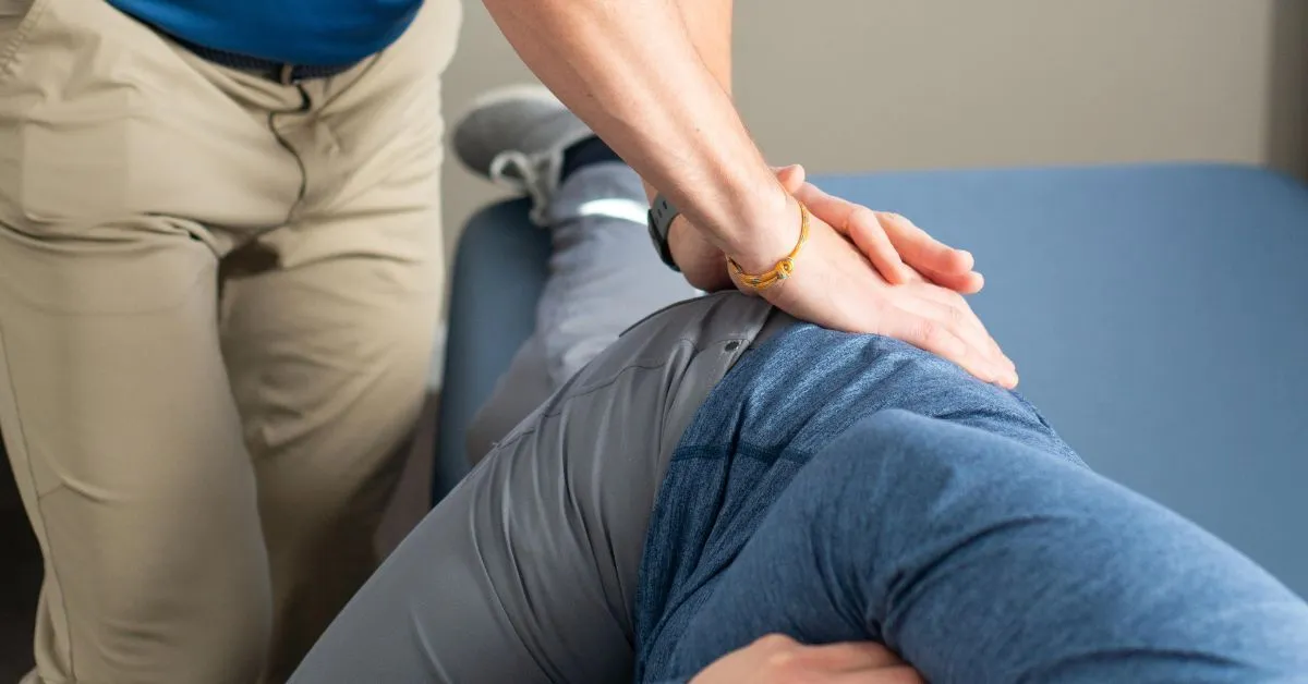 A REACH clinician in a blue shirt applying downward pressure to the glute of a side-lying patient during a hands-on treatment session