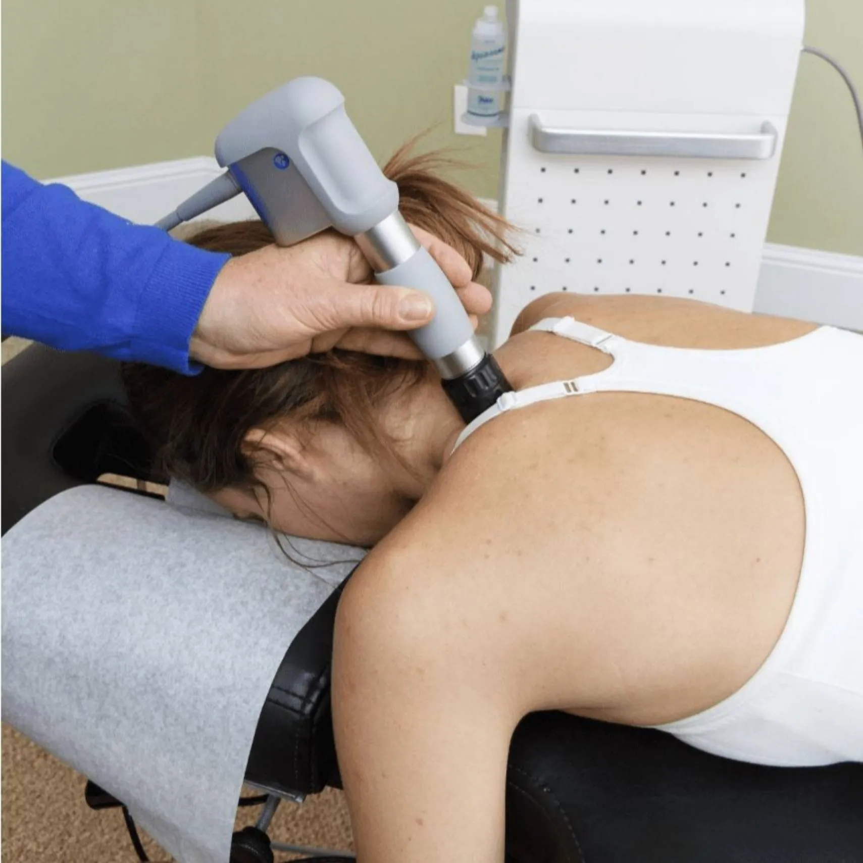 A clinician administering shockwave therapy to a patient's upper back at REACH Rehab + Chiropractic