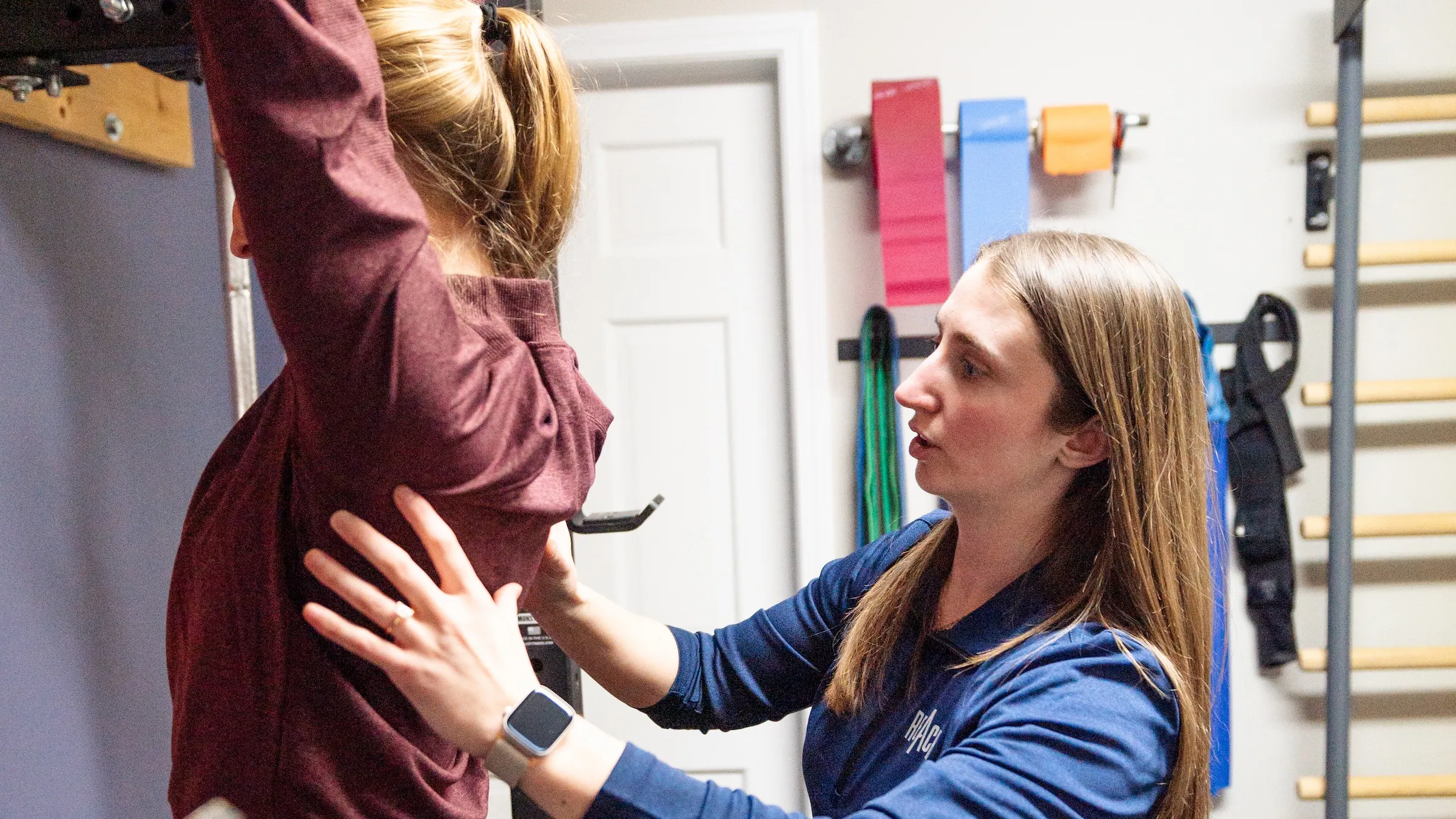 Dr. Sheridan Kent assessing a patient's overhead shoulder reach, one hand on the ribs and one on the shoulder blade, at REACH Rehab + Chiropractic, Plymouth MI