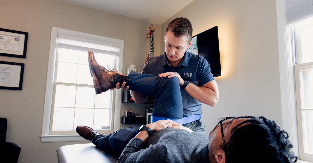 Chiropractor Helping a Patient Stretch Their Knee and Hipe While They Lay On Their Back on A Chiropractic Table | Reclaim Your Lifestyle | Discover the Fastest Path to Recovery From Injury | REACH Rehab + Chiropractic