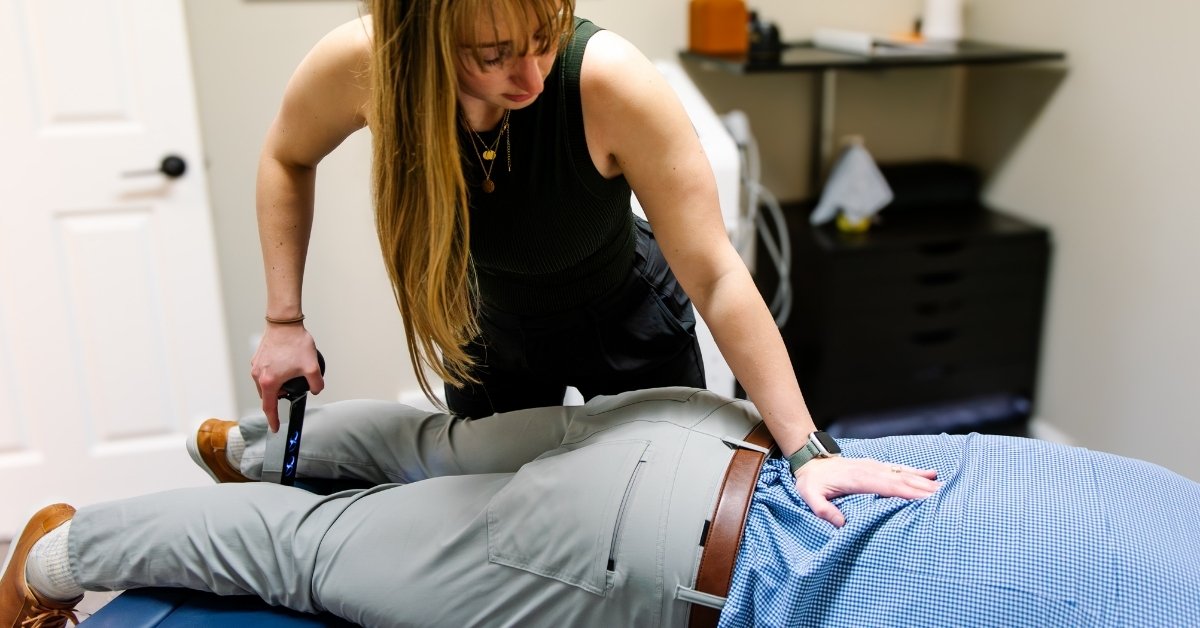 Dr. Sheridan Kent is using a flexion-distraction table for a male patient’s back while he lies face down on the Cox Table in a rehabilitation chiropractic clinic, REACH Rehab.